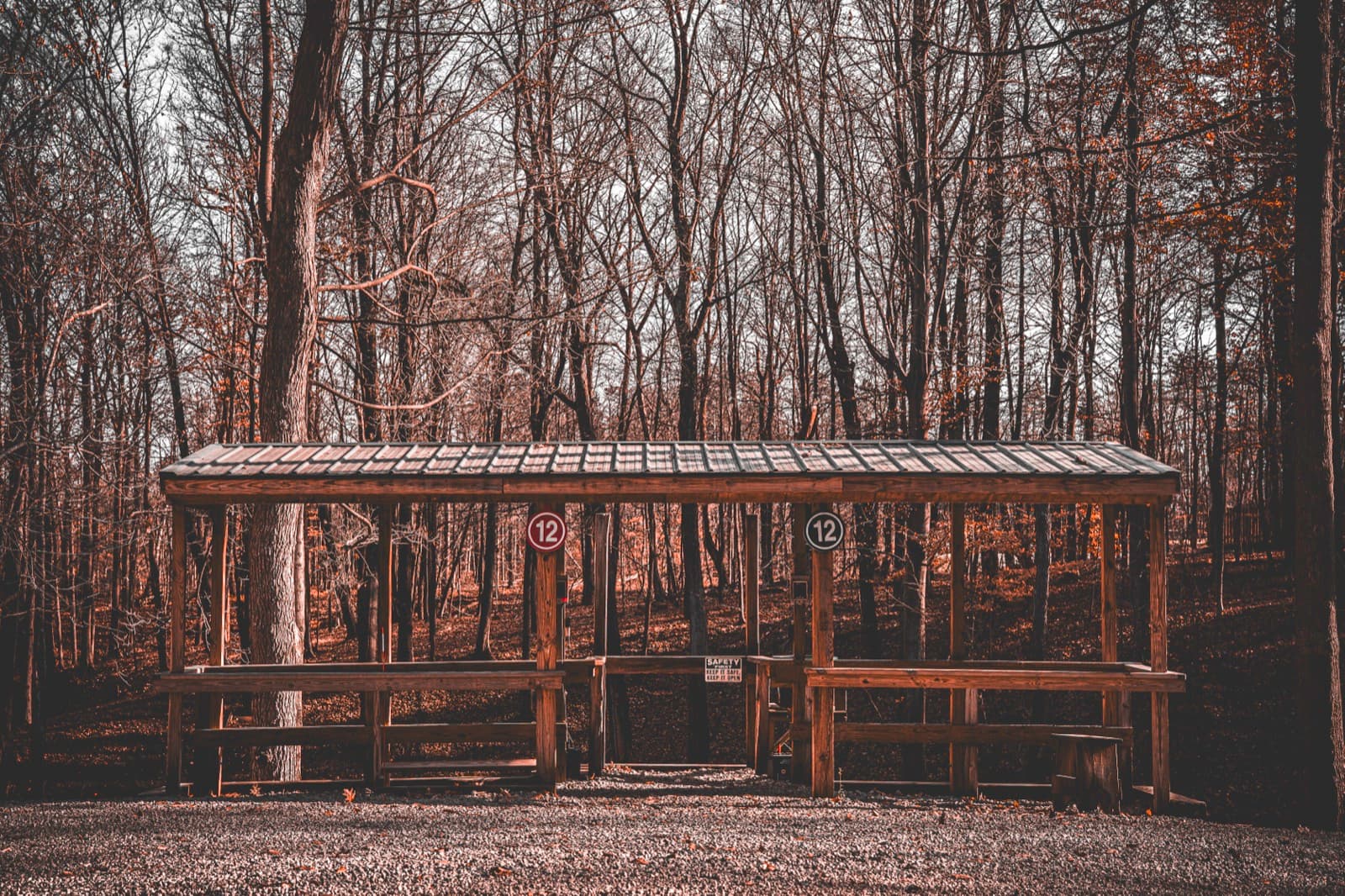 A wooded sporting clays station with numbered stands under a low roof.