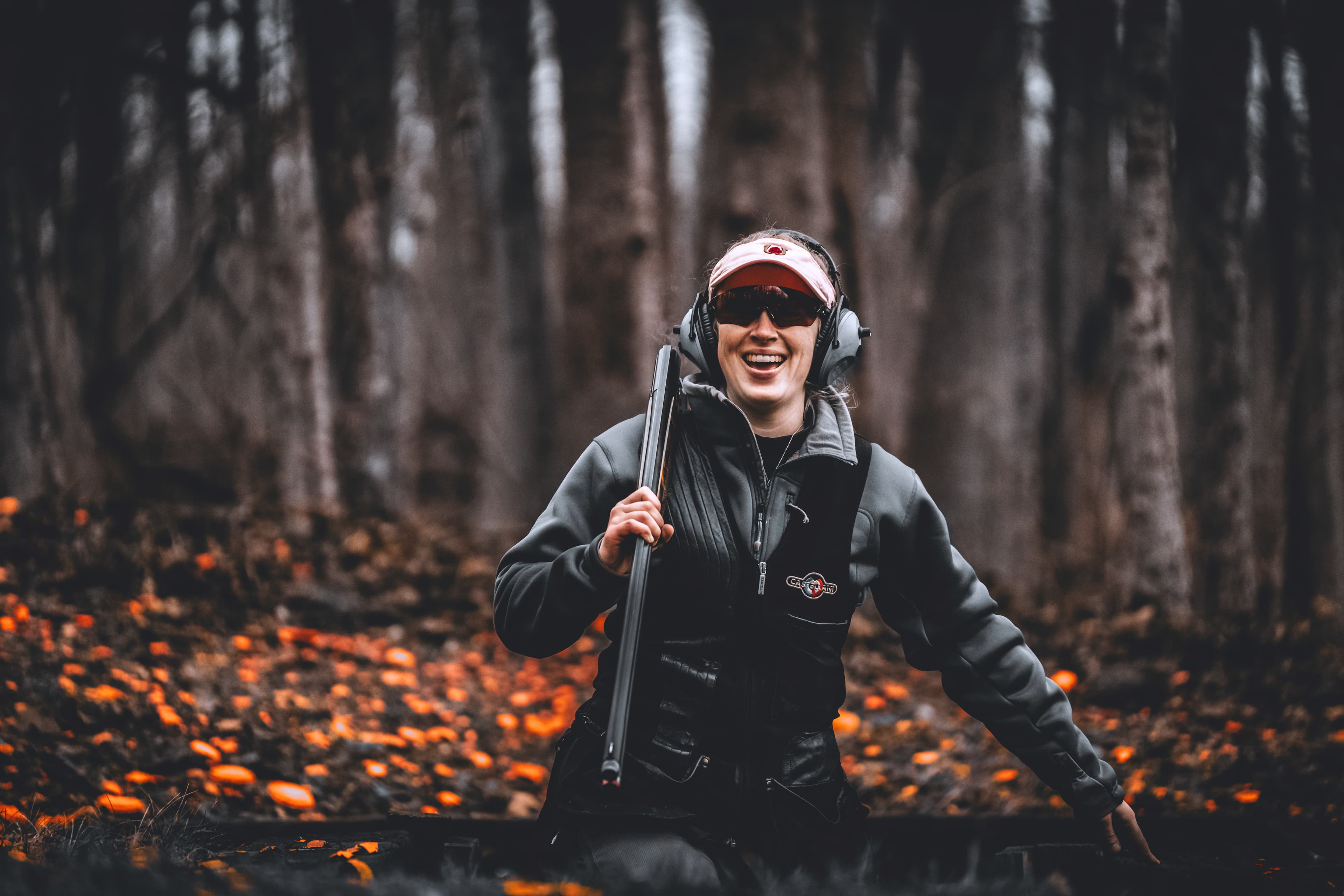 Shooter standing in a dark wooded range with orange clays scattered below.