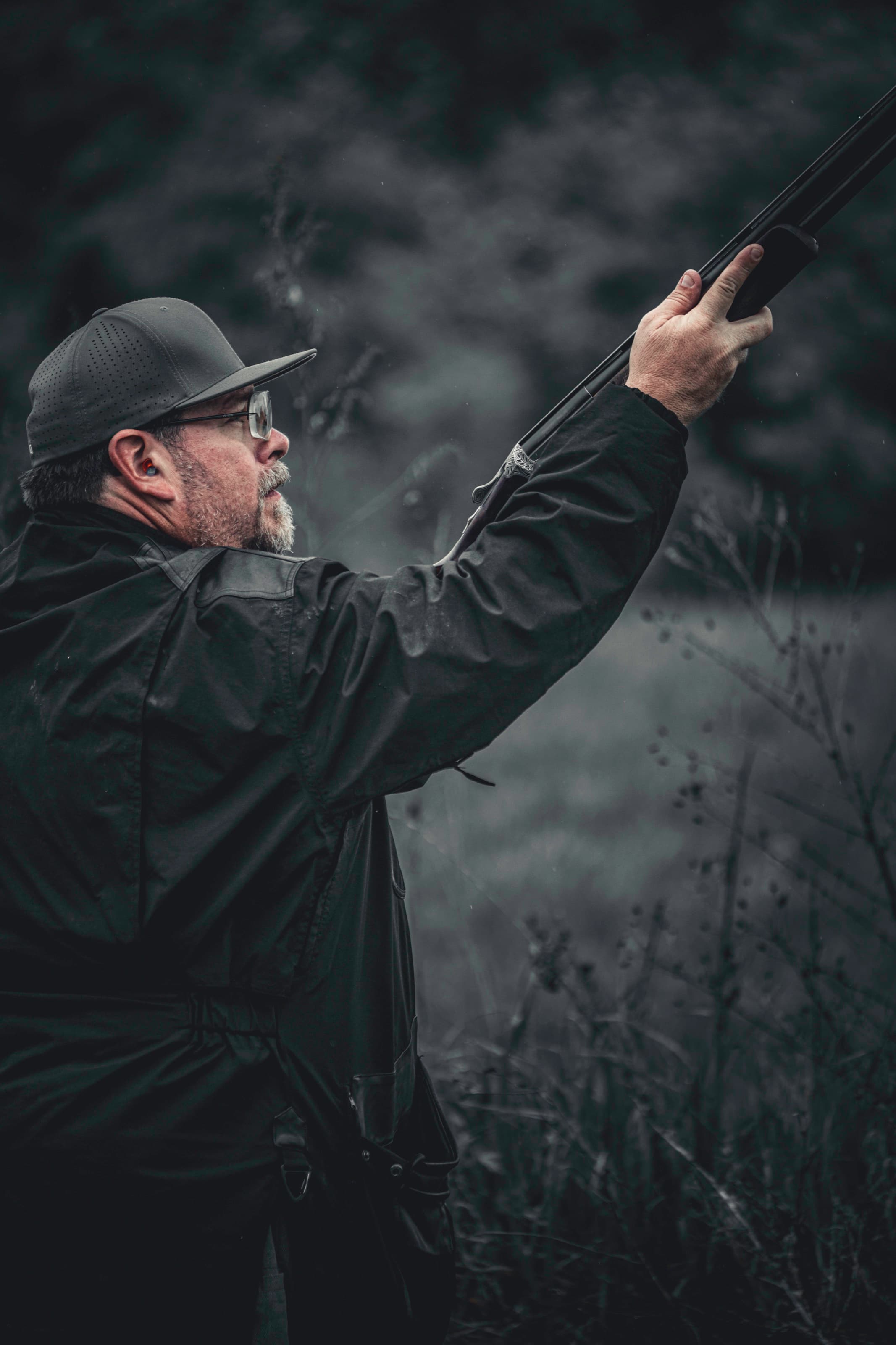 A close profile of a shooter wearing a dark cap and tinted shooting glasses.