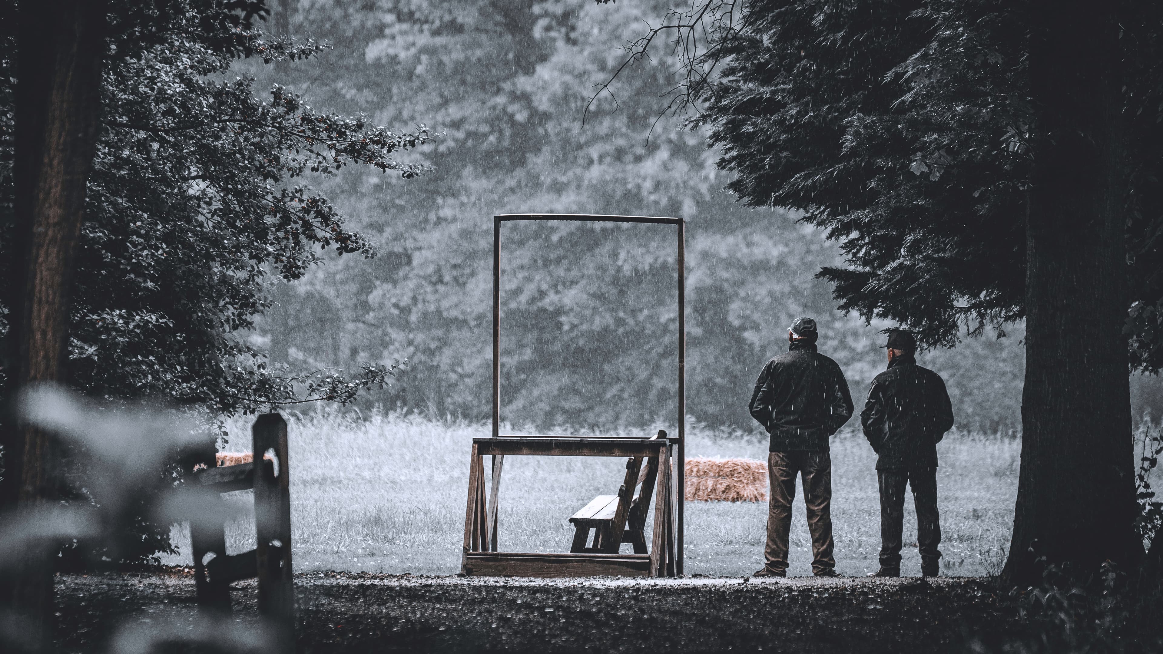 Two people standing near a rectangular field frame in heavy rain.