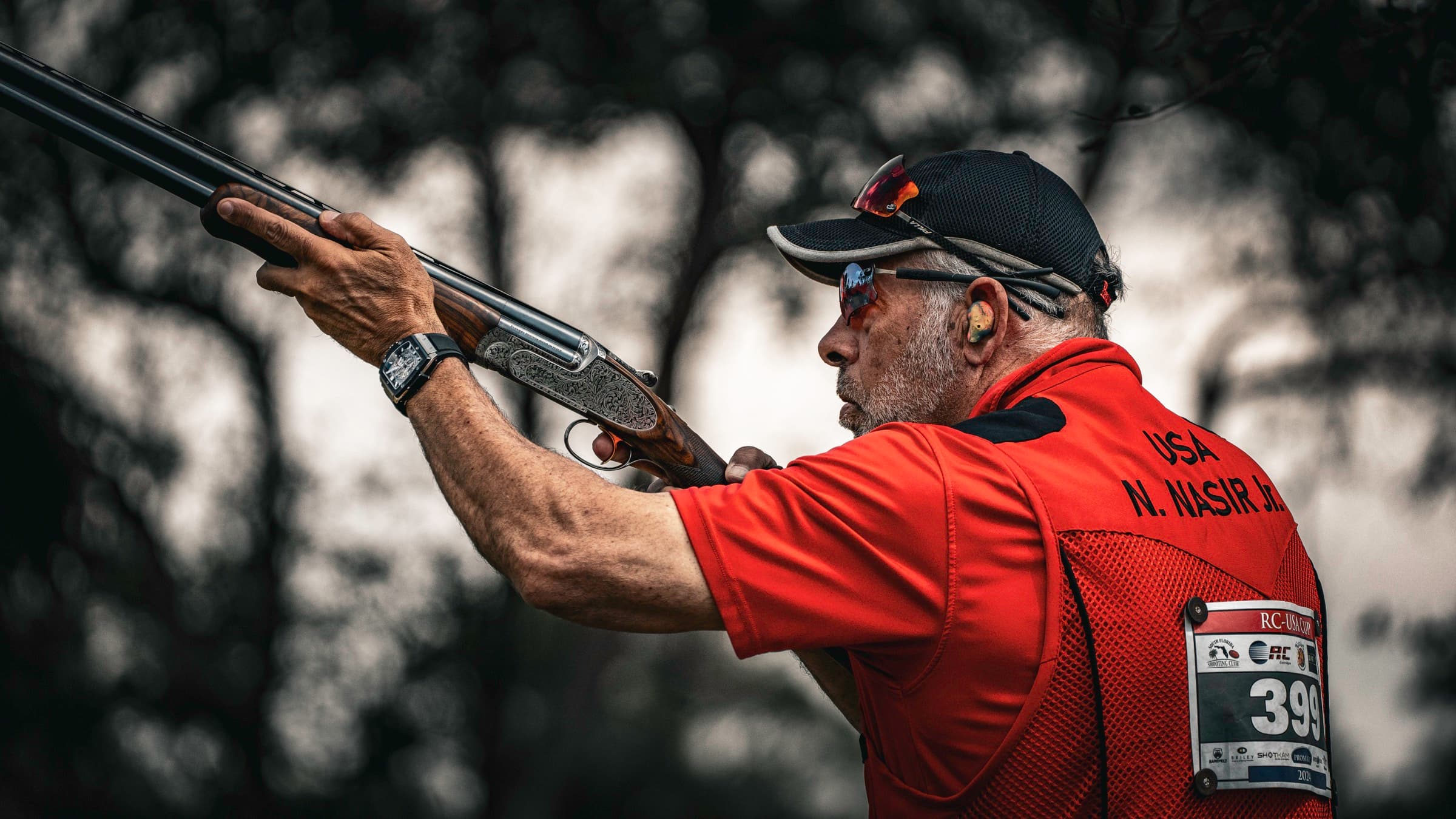 Two competitors look upward through brush and foreground blur during a sporting clays round.