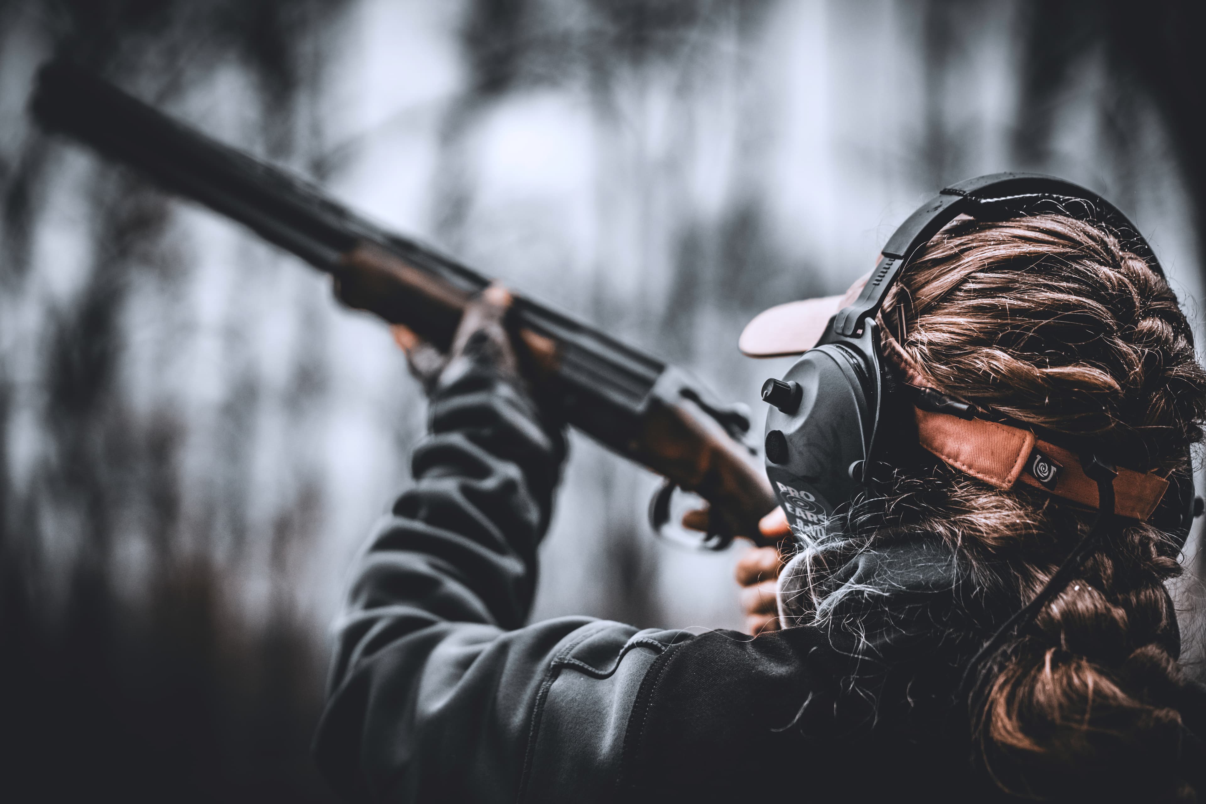 A close view from behind of a shooter raising a shotgun in a wooded field.