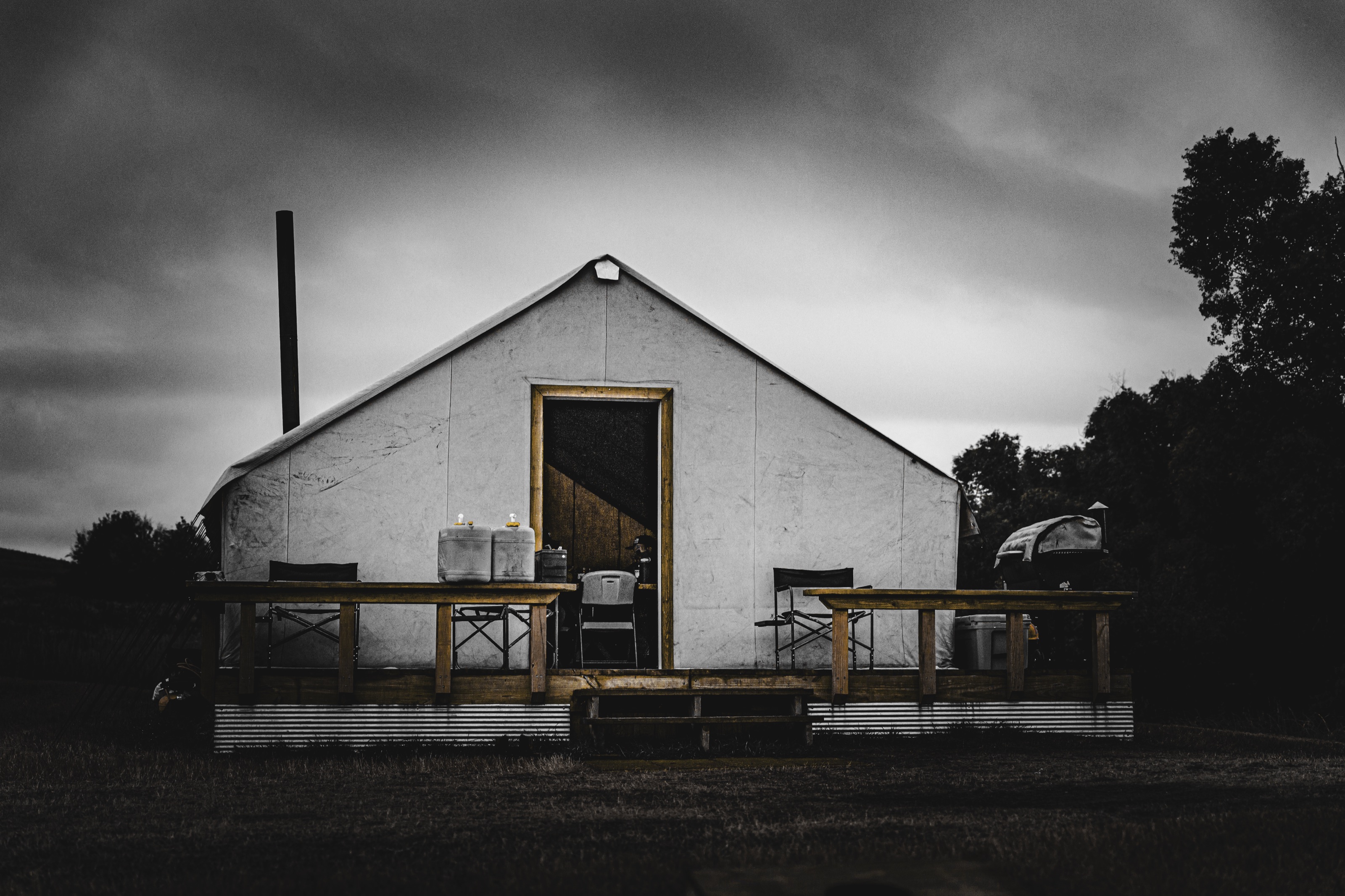 A white field tent under a gray sky with an open doorway and work tables in front.